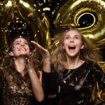 Happy gorgeous girls in stylish sexy party dresses holding gold 2022 balloon